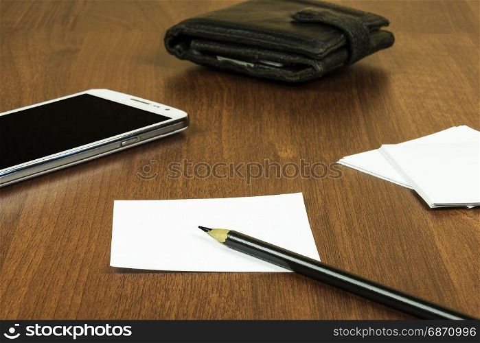 On the surface of the table lie a sheet for notes, a pencil, a smartphone and a purse