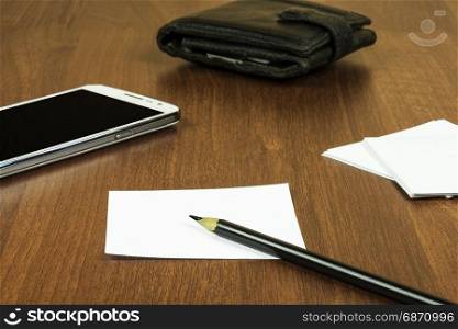 On the surface of the table lie a sheet for notes, a pencil, a smartphone and a purse