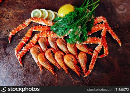 On the table are shrimp, crab, lemon and herbs. Table of reddish color.