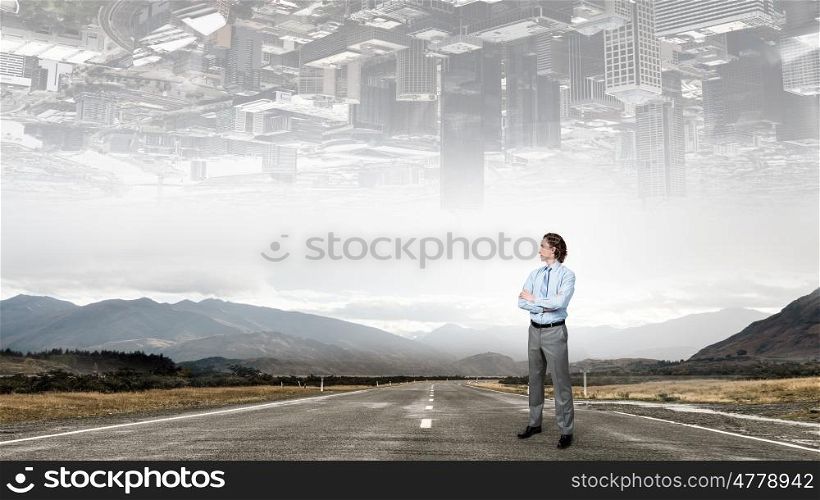 On the way to success. Self assured businessman standing on road with arms crossed on chest