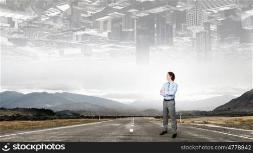 On the way to success. Self assured businessman standing on road with arms crossed on chest