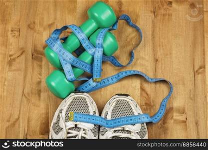 On the wooden floor are two dumbbells, white sneakers and a centimeter