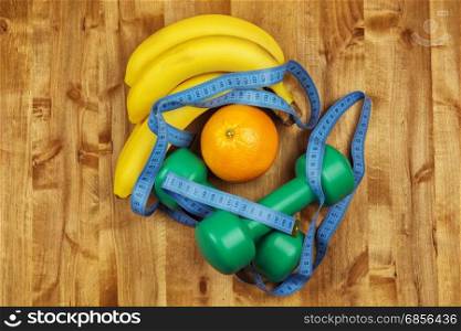 On the wooden surface are two dumbbells, centimeter, bananas and orange