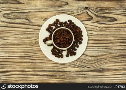 On the wooden surface is a white saucer and coffee cup with coffee beans