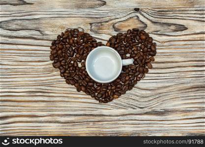 On the wooden surface with coffee beans there is a heart and inside there is an empty coffee cup