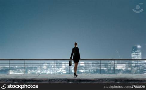 On top of business. Back view of businesswoman standing on roof looking at city