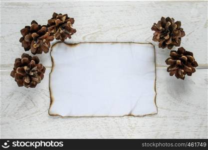 On white wooden boards, a sheet of paper burned along the edges, forest cones around the edges. Leaving space for text. Concept background.. On white wooden boards, a sheet of paper burned along the edges, forest cones around the edges. Leaving space for text.