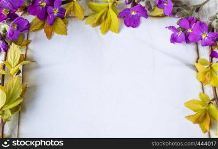On white wooden boards, branches with yellow sheets and purple flowers, a white sheet of paper burned at the edges, leaving room for text. Concept background.. On white wooden boards, branches with yellow sheets and purple flowers, a white sheet of paper burned at the edges, leaving room for text.