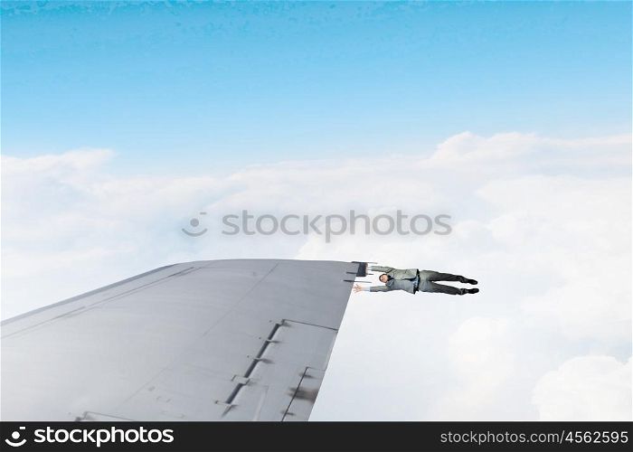 On wing of flying airplane. Young businessman flying on edge of airplane wing