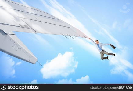 On wing of flying airplane. Young businessman flying on edge of airplane wing