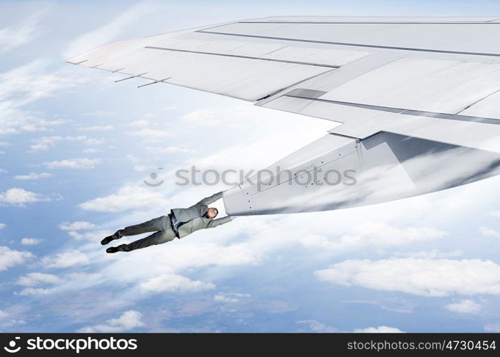 On wing of flying airplane. Young businessman flying on edge of airplane wing