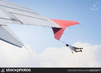 On wing of flying airplane. Young businessman flying on edge of airplane wing