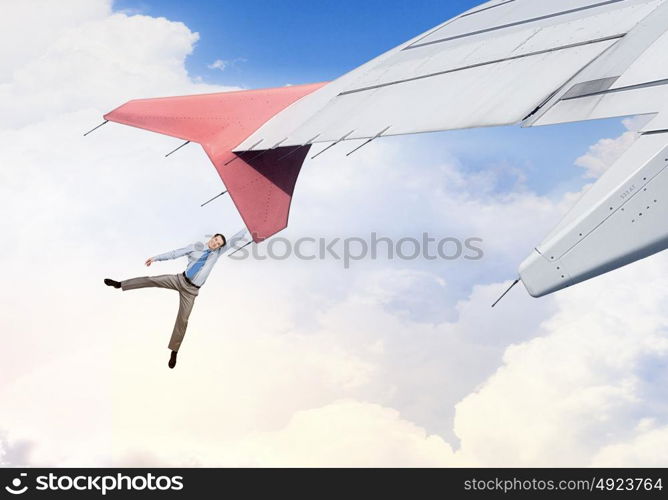 On wing of flying airplane. Young businessman flying on edge of airplane wing