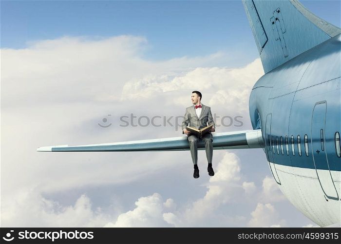 On wing of flying airplane. Young businessman sitting on wing of airplane and reading book
