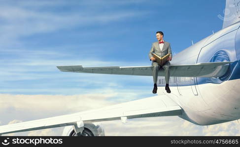 On wing of flying airplane. Young businessman sitting on wing of airplane and reading book