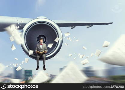 On wing of flying airplane. Young businessman sitting on wing of airplane and reading book