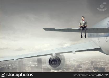 On wing of flying airplane. Young businessman sitting on wing of airplane and reading book