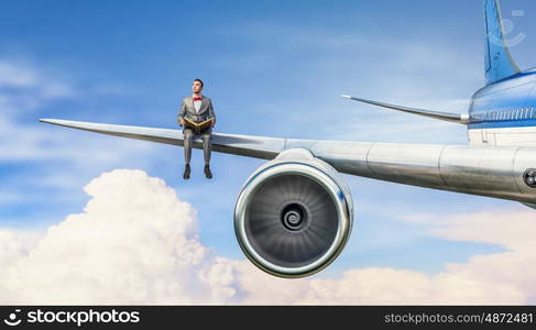 On wing of flying airplane. Young businessman sitting on wing of airplane and reading book