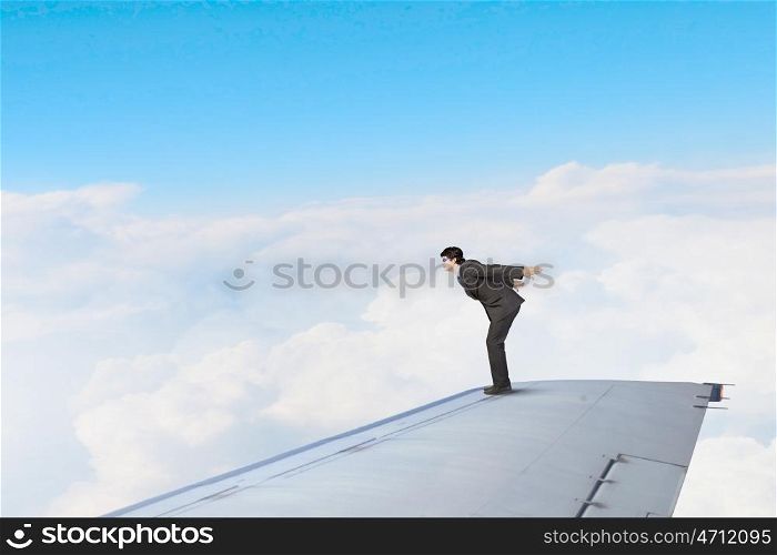 On wing of flying airplane. Young businessman standing on edge of airplane wing