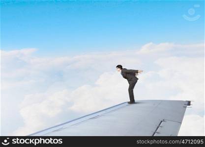 On wing of flying airplane. Young businessman standing on edge of airplane wing