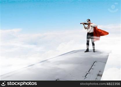 On wing of flying airplane. Young businessman super hero on edge of airplane wing play violin
