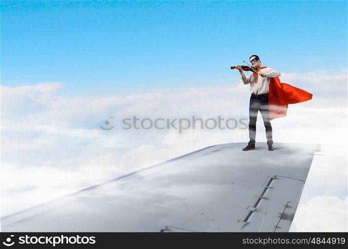 On wing of flying airplane. Young businessman super hero on edge of airplane wing play violin
