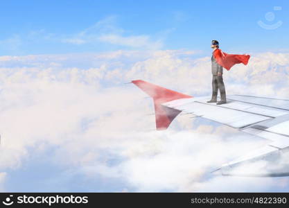 On wing of flying airplane. Young businessman super hero on edge of airplane wing