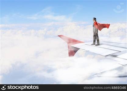 On wing of flying airplane. Young businessman super hero on edge of airplane wing