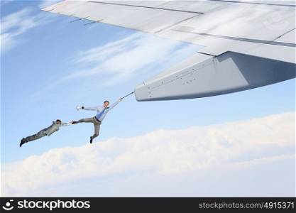 On wing of flying airplane. Young businessmen flying on edge of airplane wing