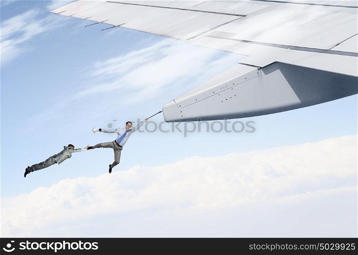 On wing of flying airplane. Young businessmen flying on edge of airplane wing