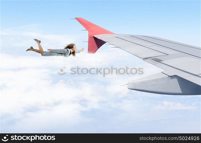 On wing of flying airplane. Young businesswoman flying on edge of airplane wing