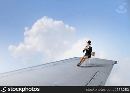 On wing of flying airplane. Young businesswoman sitting on edge of airplane wing