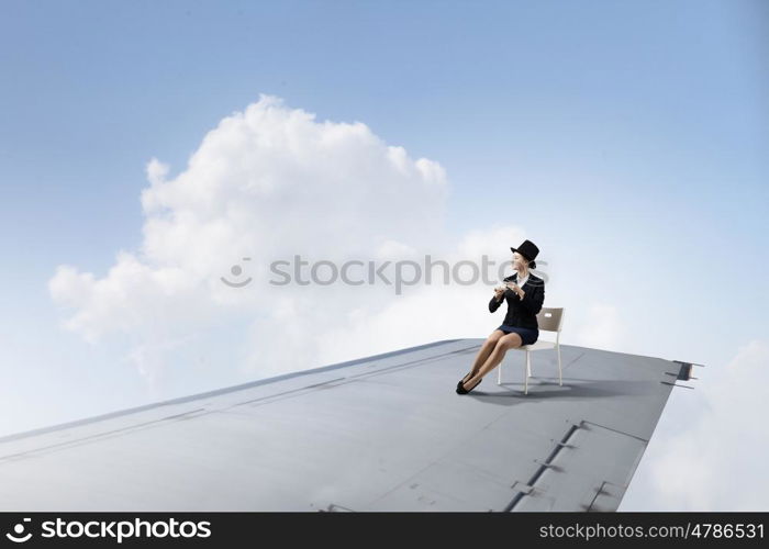 On wing of flying airplane. Young businesswoman sitting on edge of airplane wing