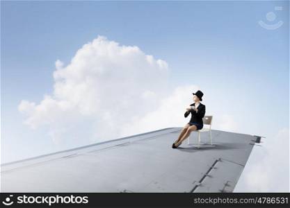 On wing of flying airplane. Young businesswoman sitting on edge of airplane wing