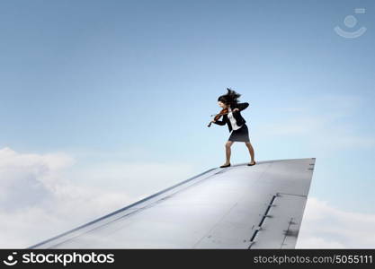 On wing of flying airplane. Young businesswoman standing on edge of airplane wing and play violin