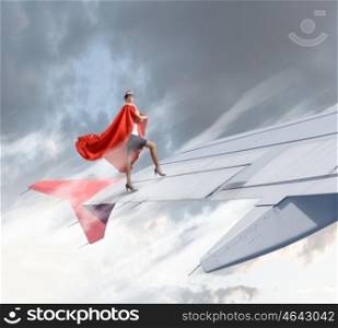 On wing of flying airplane. Young businesswoman standing on edge of airplane wing