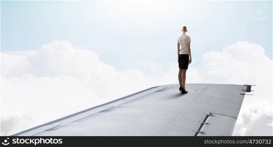 On wing of flying airplane. Young businesswoman standing on edge of airplane wing