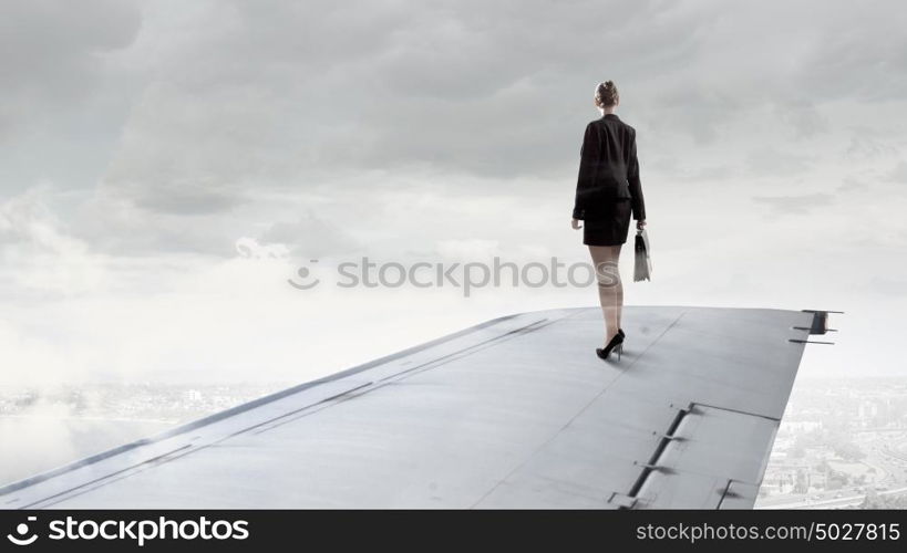 On wing of flying airplane. Young businesswoman standing on edge of airplane wing