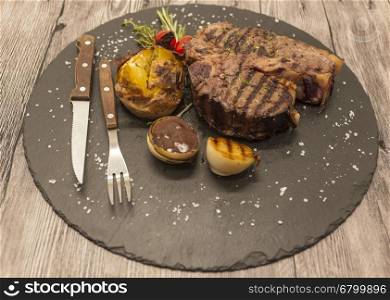 On wooden table background juicy beef steak medium rare on a stone baked potatoes and barbecue sauce and large sea salt with fork and knife.. On wooden table background juicy beef steak medium rare on a stone baked potatoes and barbecue sauce and large sea salt with fork and knife