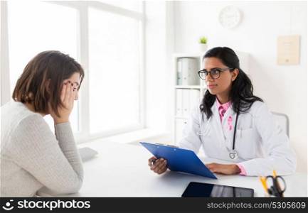oncology and breast cancer concept - female doctor with pink awareness ribbon and sad patient at hospital. doctor with pink awareness ribbon and sad patient