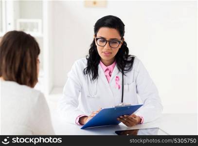 oncology and breast cancer concept - female doctor with pink awareness ribbon and patient at hospital. doctor with pink awareness ribbon and patient