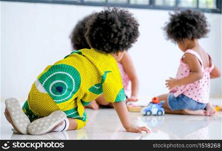 One African boy look at two girls play toys together and look like he want to play with them.