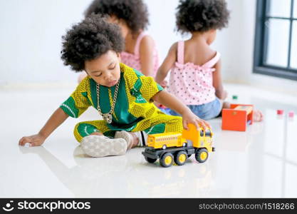 One African mixed race boy is playing with truck toys in front of the other girls and look enjoy and happy with this activity.