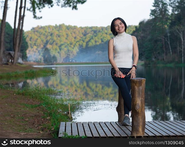 One asian lady sitting on wooden pole at the pier in Pang Ung lake, Mae Hong Son province, Thailand.