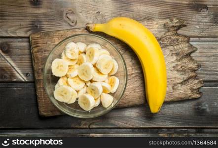 One banana and banana slices in a glass plate on an old cutting Board. On a black wooden background.. One banana and banana slices in a glass plate on an old cutting Board.