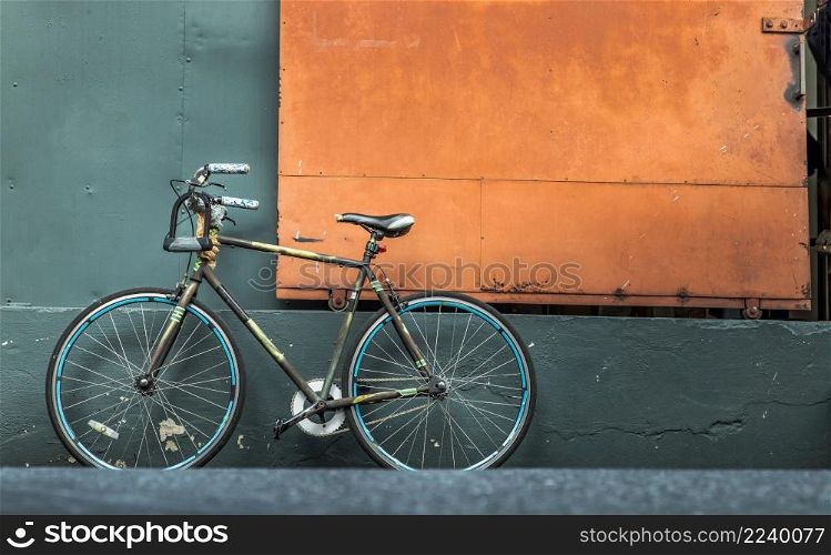 One bicycle in front of steel orange door with green wall of warehouse. Copy space, Selective focus.