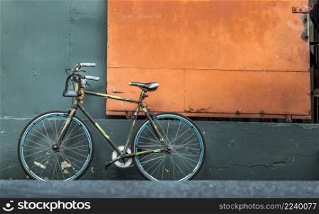 One bicycle in front of steel orange door with green wall of warehouse. Copy space, Selective focus.