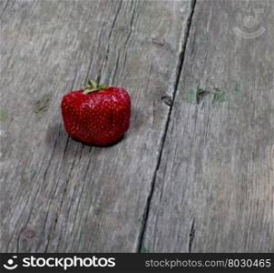 one big strawberry on a wooden table, a berry subject