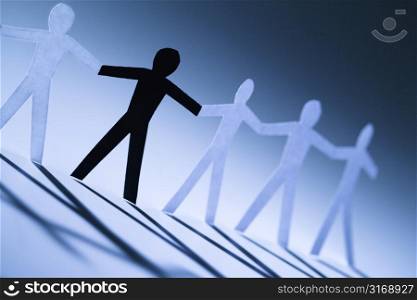 One black cutout paper person holding hands with group of white people.