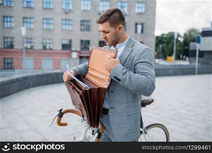One businessman biking in suit with briefcase in downtown. Business person riding on eco transport on city street. One businessman biking in suit with briefcase